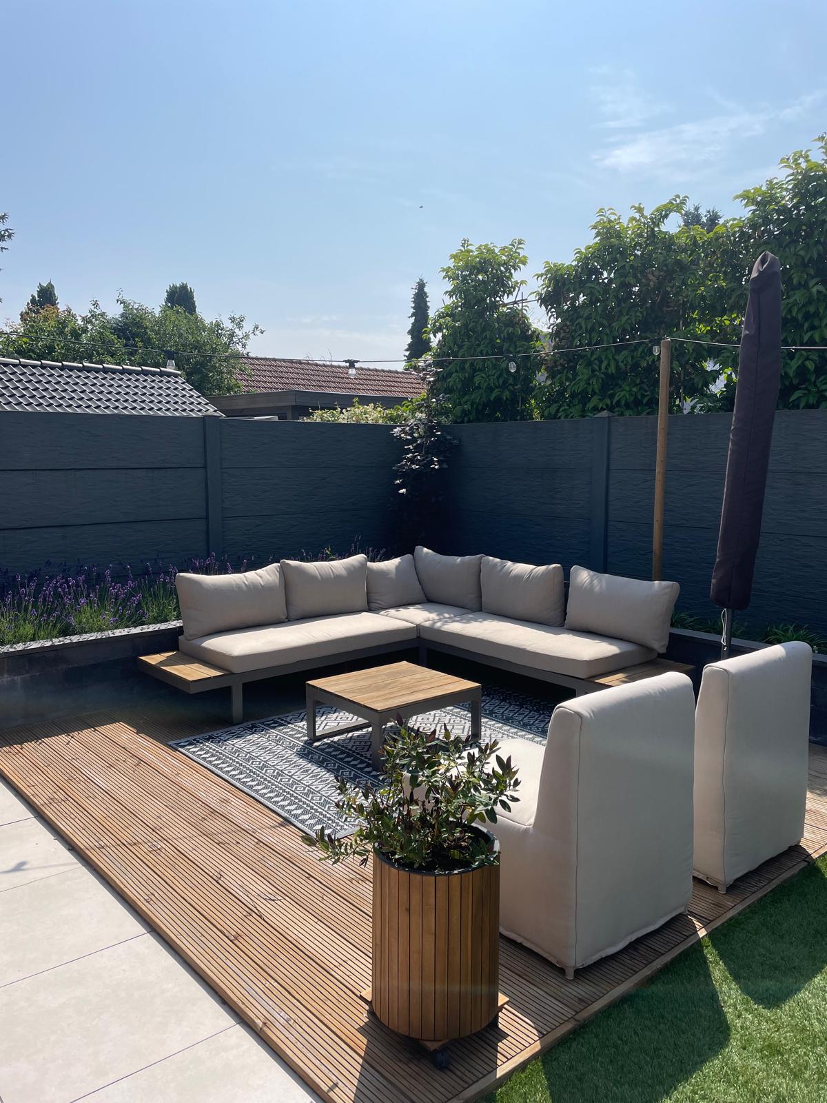 Loungebank en twee stoelen op een houten vlonder in een tuin met een zwarte schutting